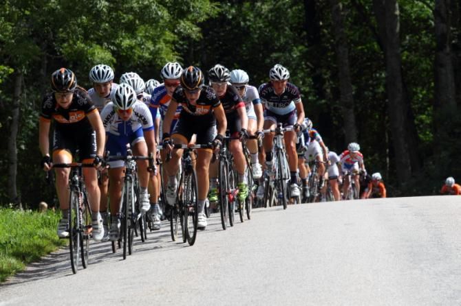 The bunch crests a hill out of a corner, an accleration forces a long line of riders