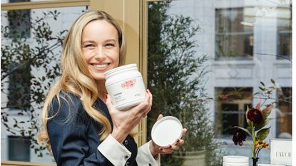 brie larson smiling and holding a white plastic jug