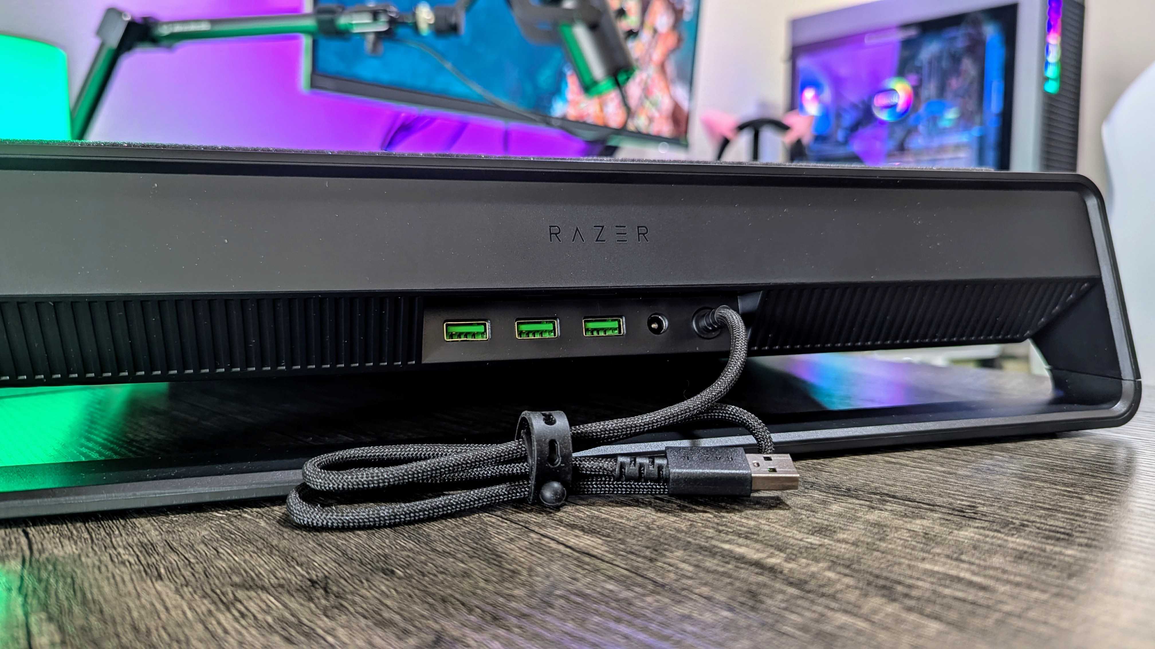 A almofada de resfriamento do laptop Razer na mesa, vista por trás, revela as três portas USB Type-A 2.0, a porta de alimentação DC de 36 W e o cabo de conexão.