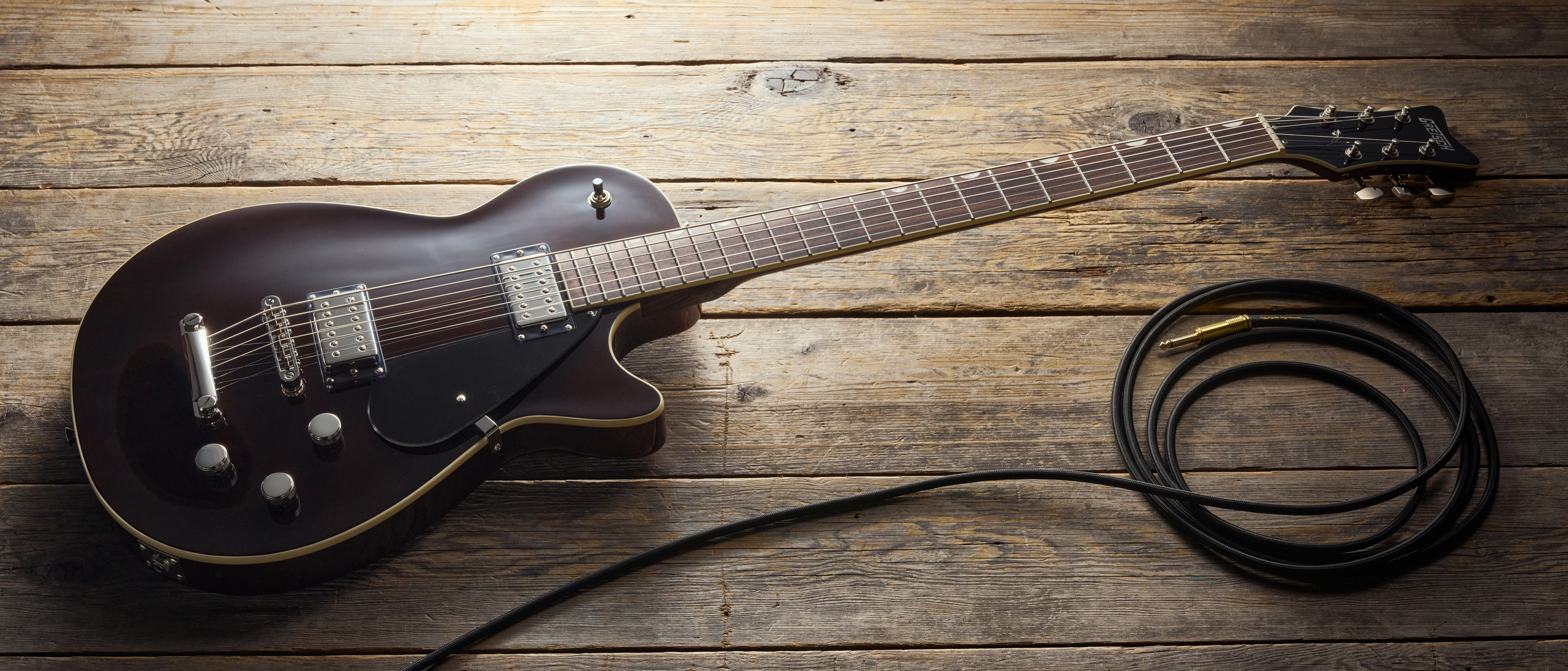 A Gretsch Electromatic Jet Baritone electric guitar on a wooden floor with a guitar cable