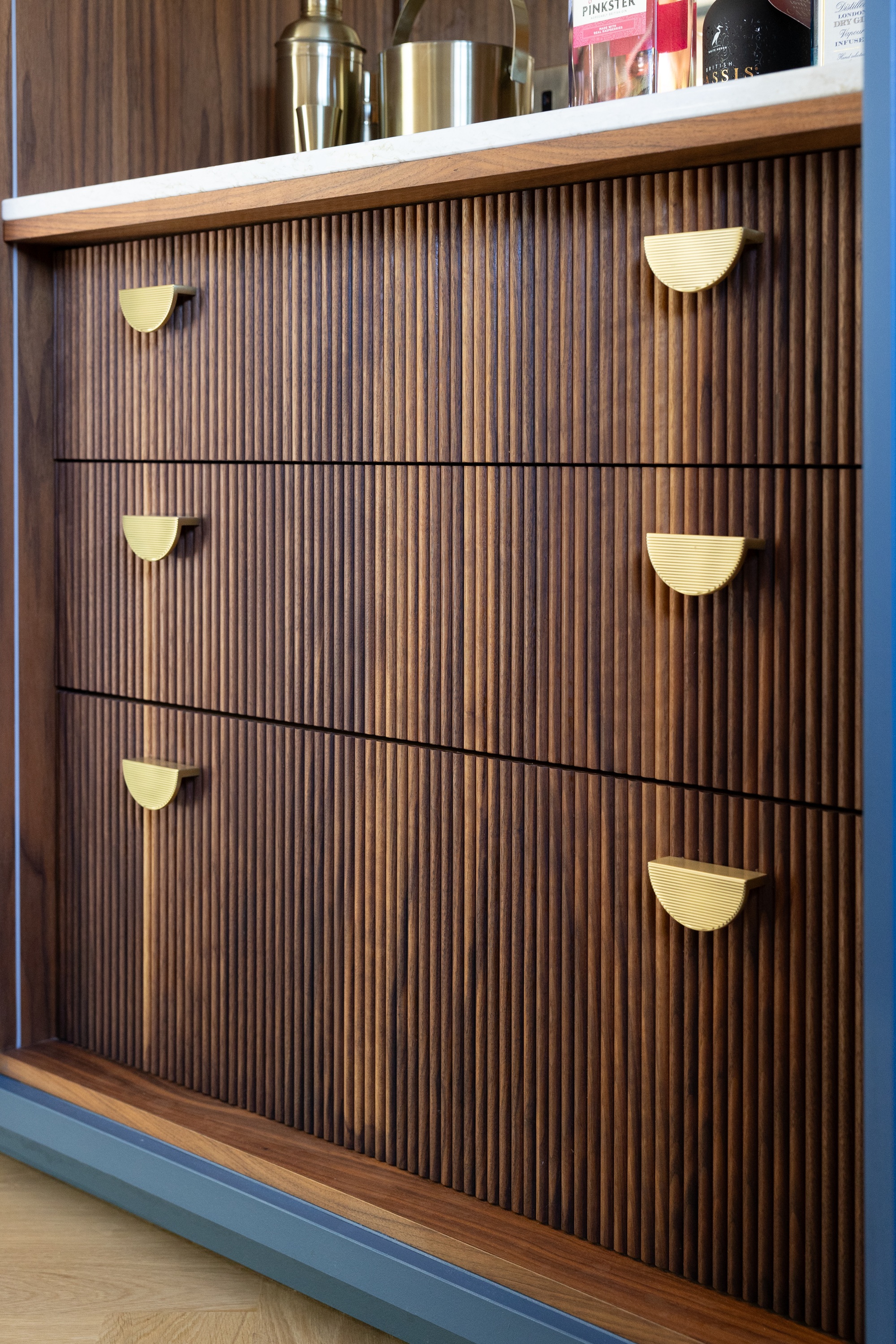 a modern art deco inspired kitchen with a wood, gold and blue color palette, with an arched ranger cooker hood and fluted island design
