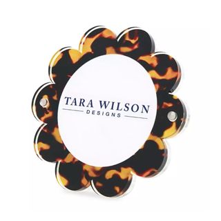 A brown and orange tortoise shell patterned frame with a scalloped design and a white middle with blue writing saying 'Tara Wilson Designs'
