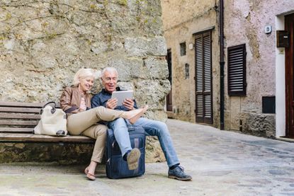 A mature couple sit on a bench looking at a digital notepad.