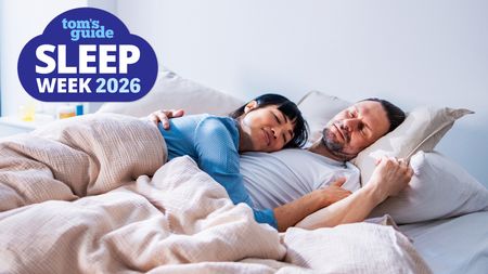 A woman dressed in a blue night shirt sleeps peacefully on her partner's chest, as he sleeps with his head on a stone colored bed pillow. In the top left hand corner is a blue Tom's Guide Sleep Awareness Week 2026 logo.