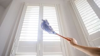 person dusting white blinds high-up