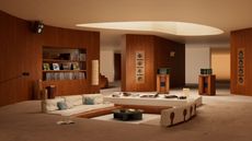 Image of a large, spacious room that is covered in carpet and has a conversation pit in the center. There are low white sofas and a white bar with a record player sound system.