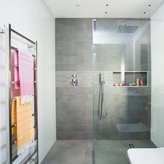 a tile bathroom with walk in shower with glass screen and a towel rail with pink and yellow towels