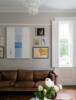 A grey living room paint color idea by Farrow & Ball with brown leather sofa and framed wall art decor