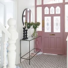 White painted hallway with a pink front door and tiled floor, with a console table and mirror on the left wall