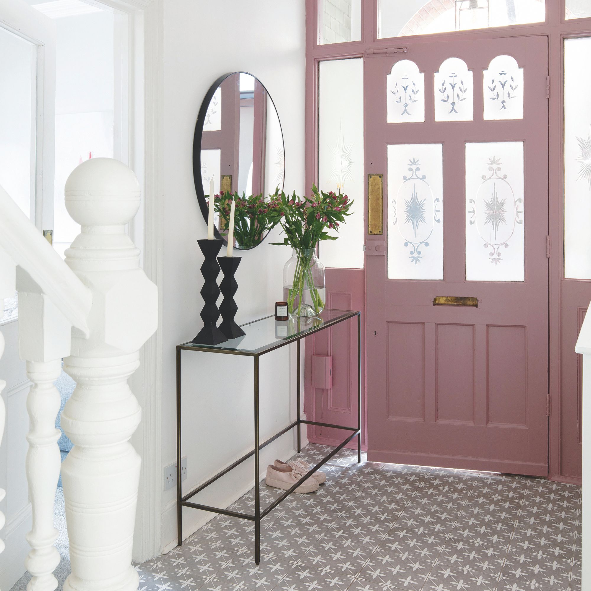 White painted hallway with a pink front door and tiled floor, with a console table and mirror on the left wall