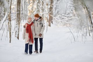 A happy couple walking in a white, snowy forest.