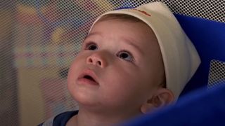 A baby looks up at a camera in his crib.