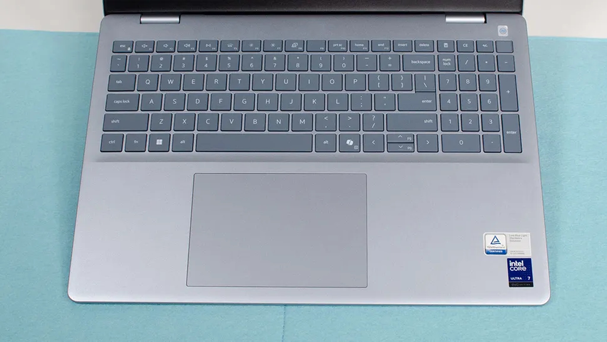 Silver laptop on a blue surface, featuring a full QWERTY keyboard, large touchpad, Intel Core i7 badge, and sleek design.