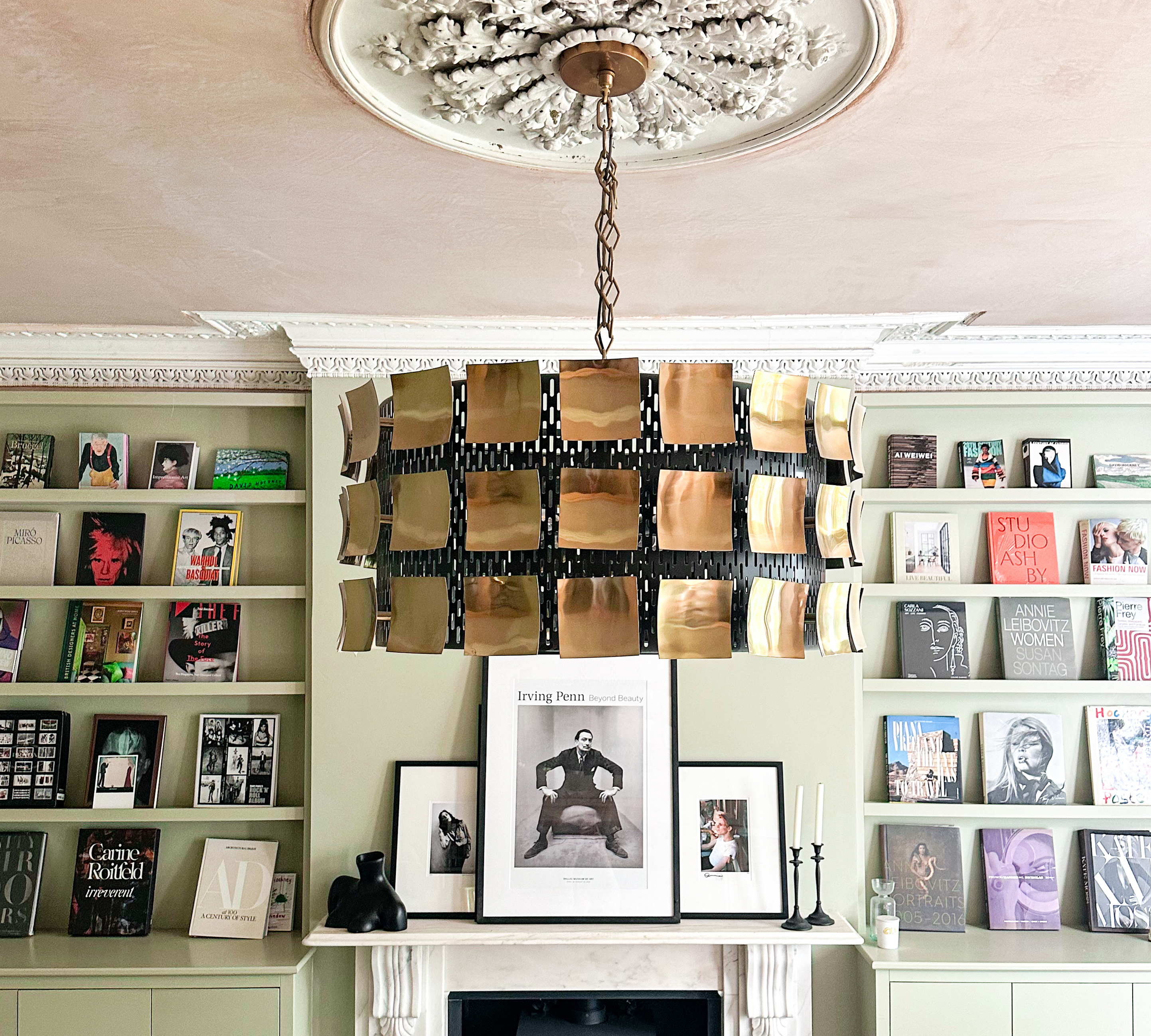 fireplace with pictures on the mantle and on shelves either side with a big chandelier