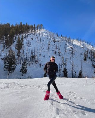 Sara wears a ski suit and red moon boots.