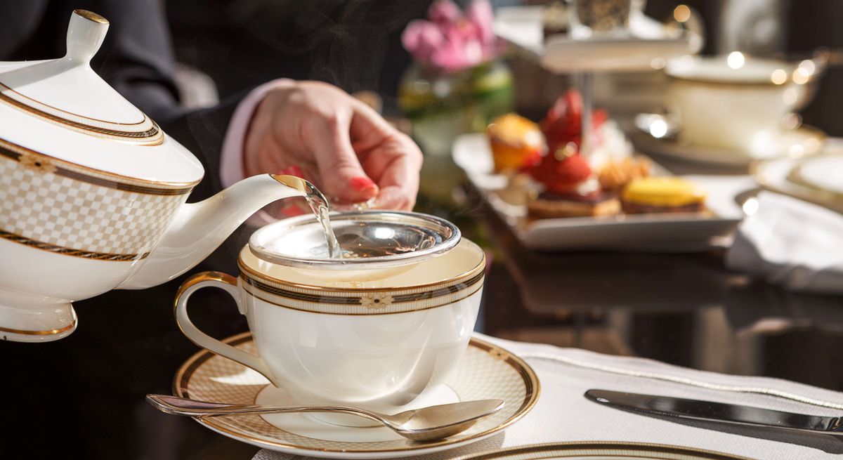 Woman ouring tea from a teapot into a cup and saucer