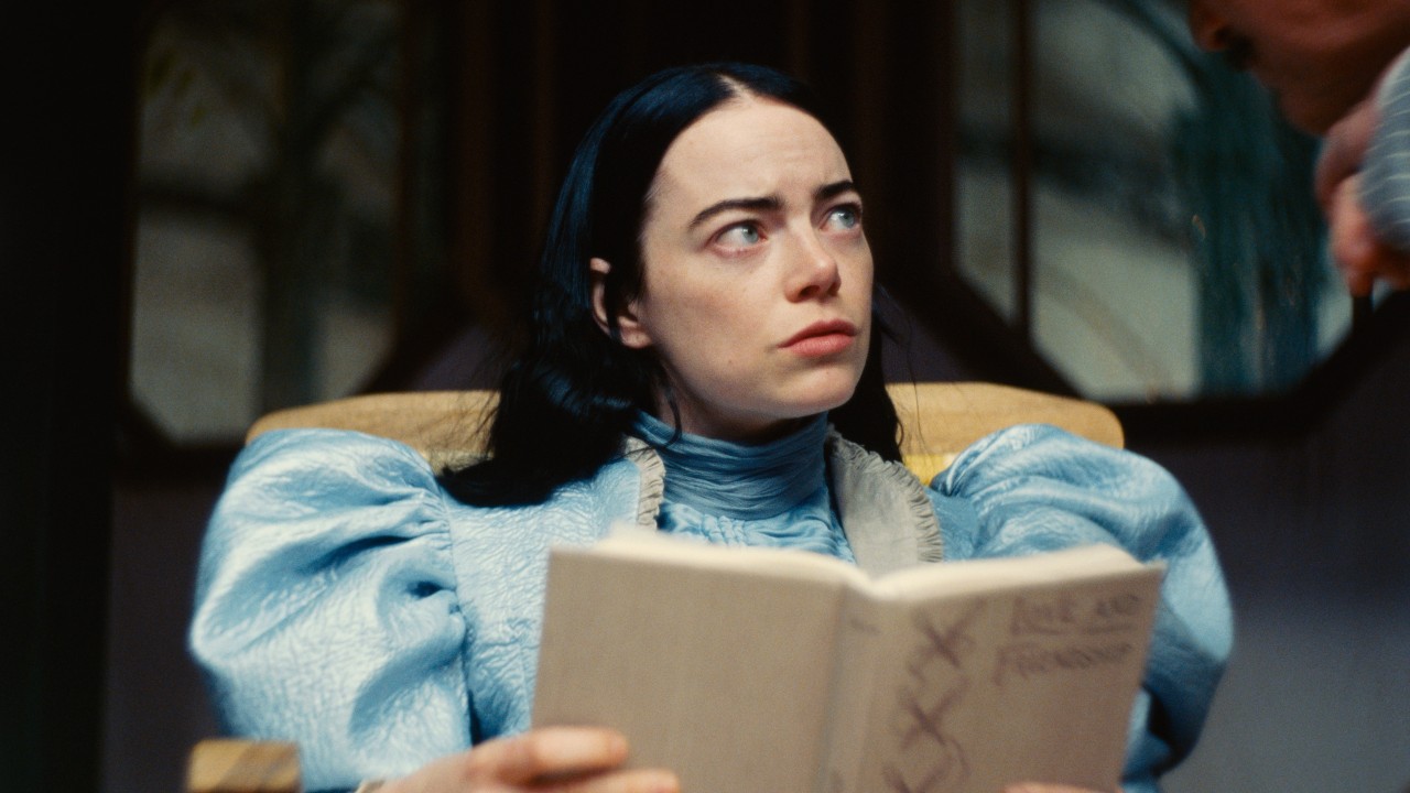 Emma Stone levanta la vista de un libro en una imagen de prensa para Poor Things.