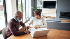 An older couple work on financial planning at their dining room table.