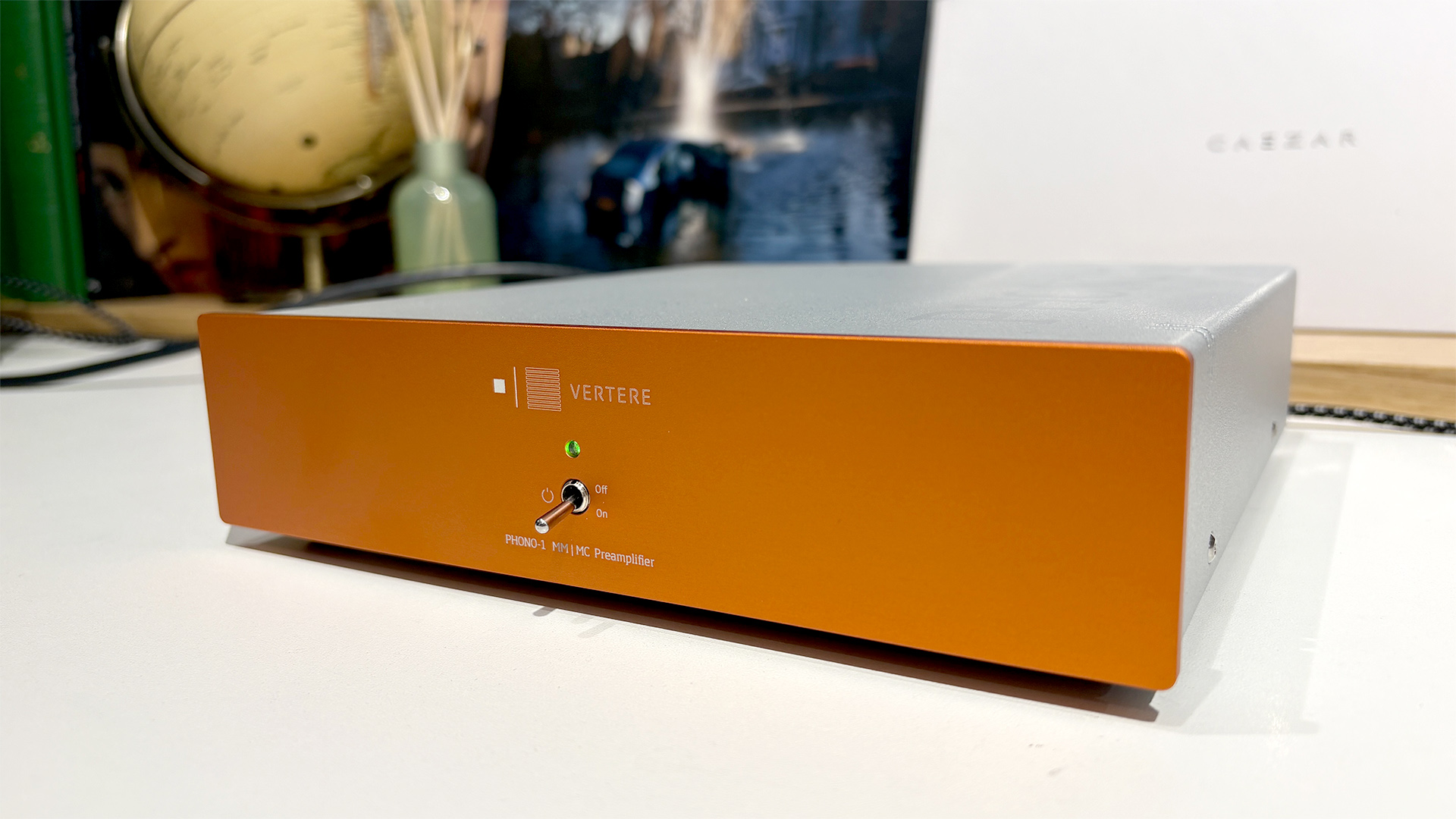 Vertere Phono-1 LX phono stage on white surface in front of busy shelf