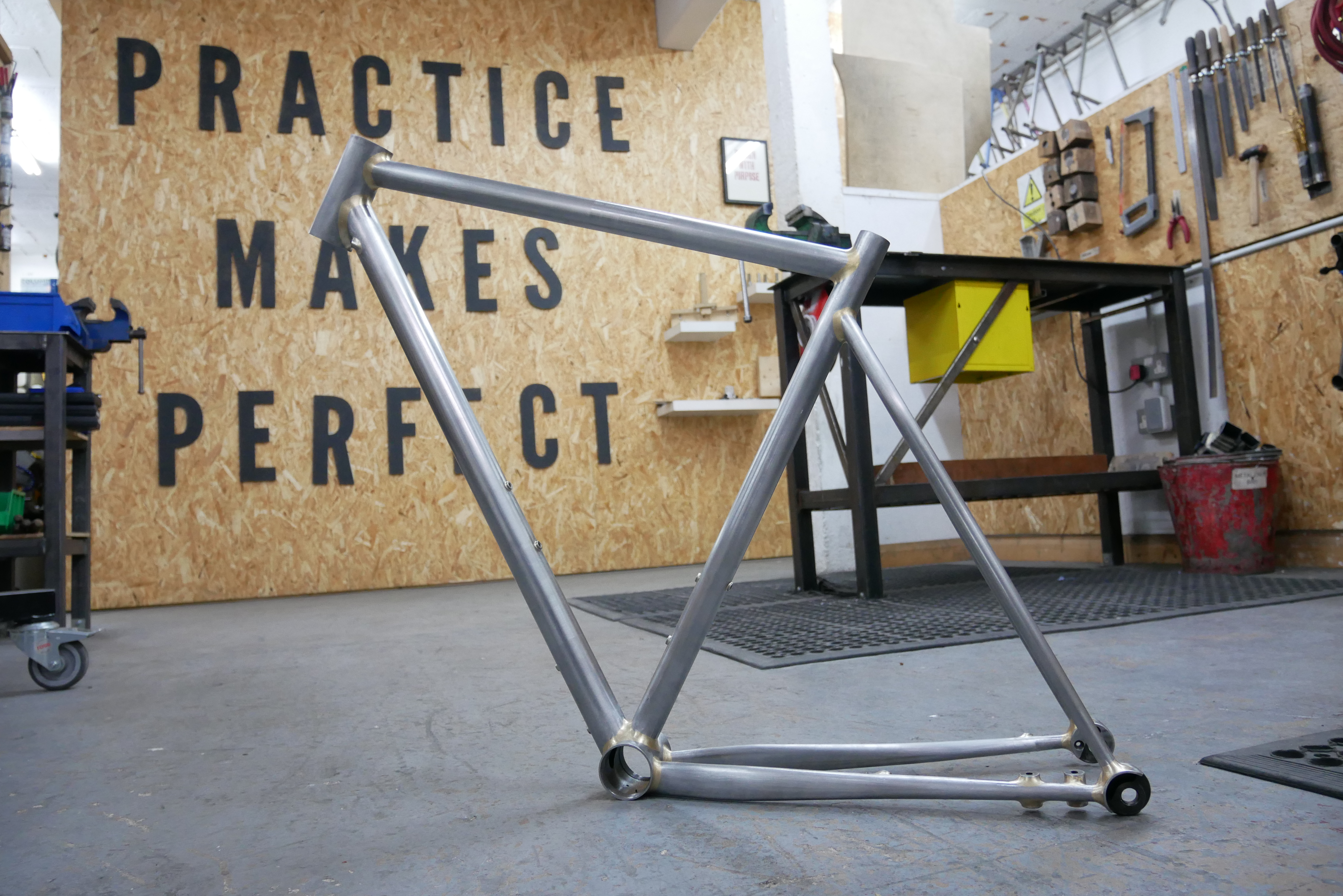 A bike frame sits in front of a sign reading 'Practice makes perfect'