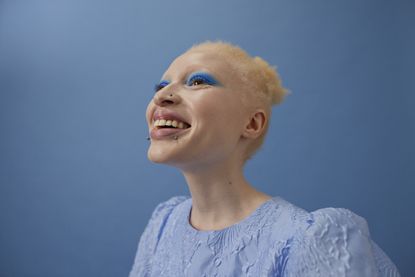 image of young woman smiling and wearing bright blue eyeshadow against a blue background