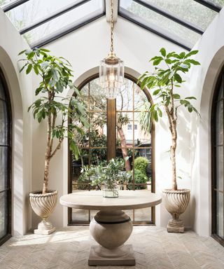 glass and gold ceiling light in room with vaulted glass ceiling, cream stone floor and walls and herringbone tiled floor