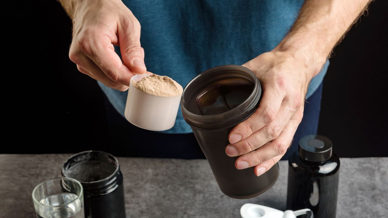 Man scooping protein powder from a tub into a flask