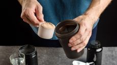 Man scooping protein powder from a tub into a flask