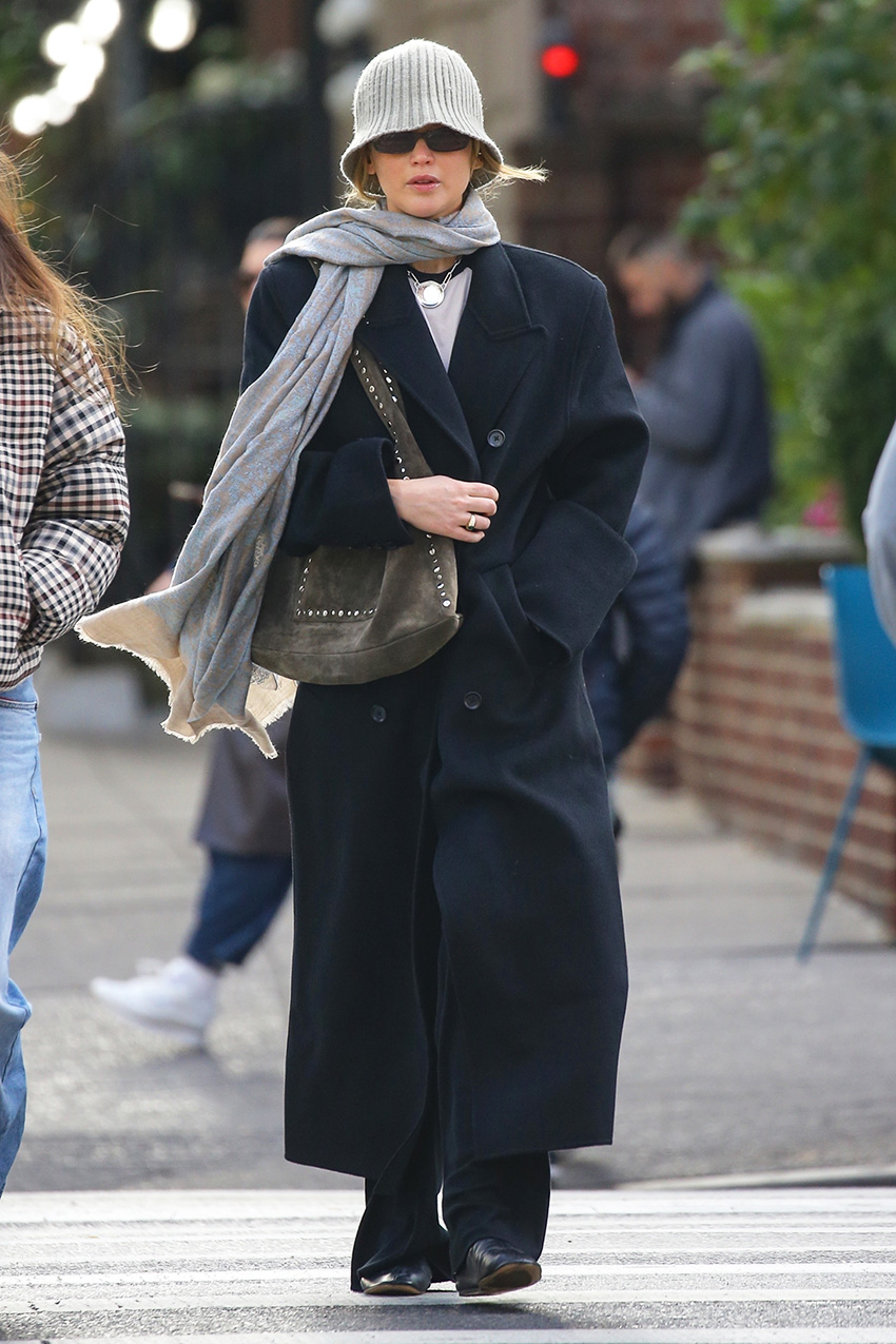 Jennifer Lawrence wearing a gray bucket hat and scarf, black coat, black flats, and a studded suede bag