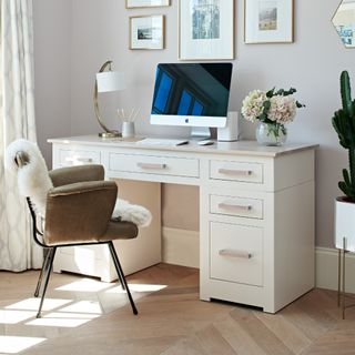 A home office with a cream desk and a vase of flowers on top