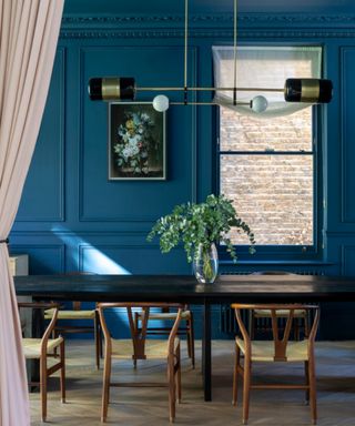 A dining room with a modern glass and brass chandelier with traditional cornicing painted in bright blue