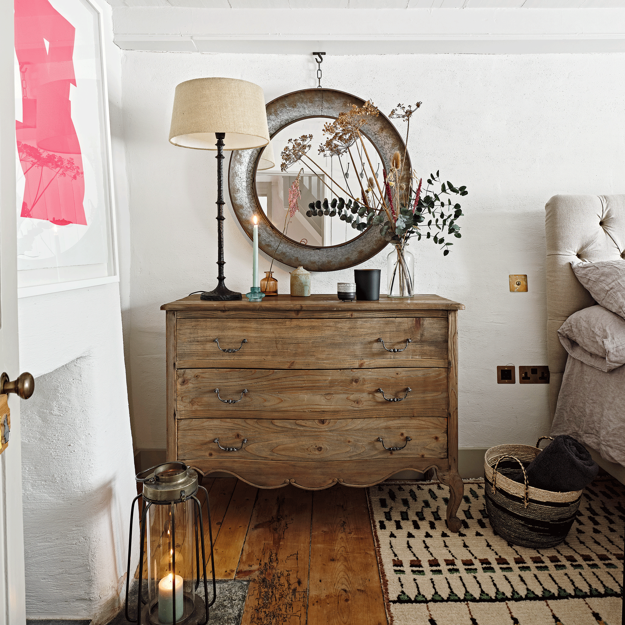 a bedroom with white walls and a large, traditional wooden chest of drawers with a large round mirror above it