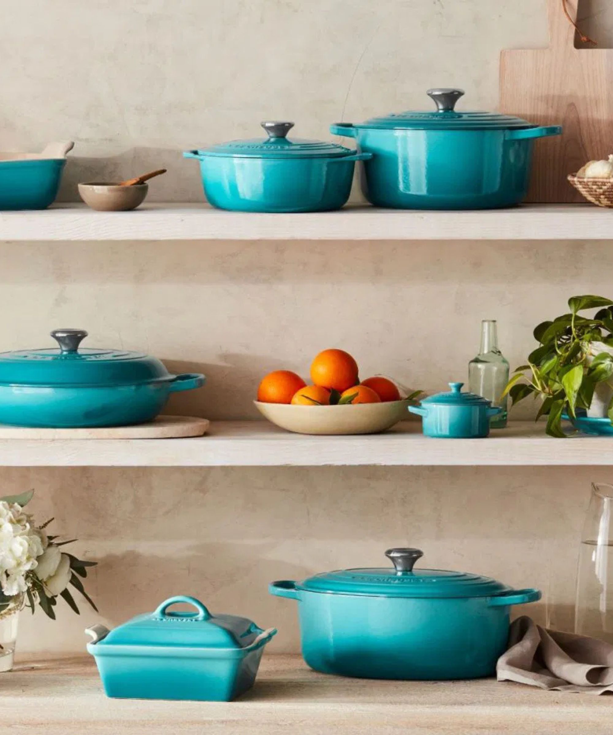 A selection of Le Creuset pieces in Caribbean on open shelving with plants and fruit bowls