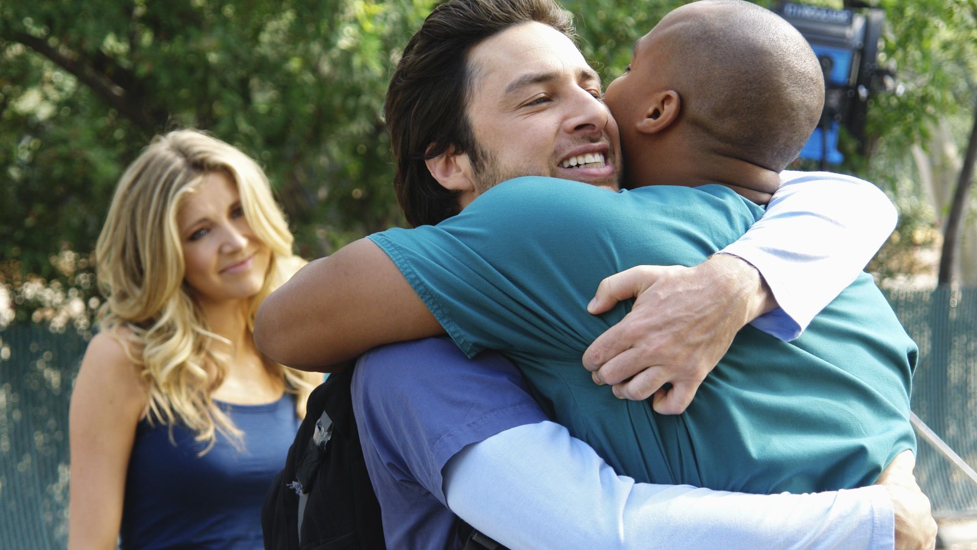 Sarah Chalke stands behind Zach Braff and Donald Faison hugging in Scrubs finale
