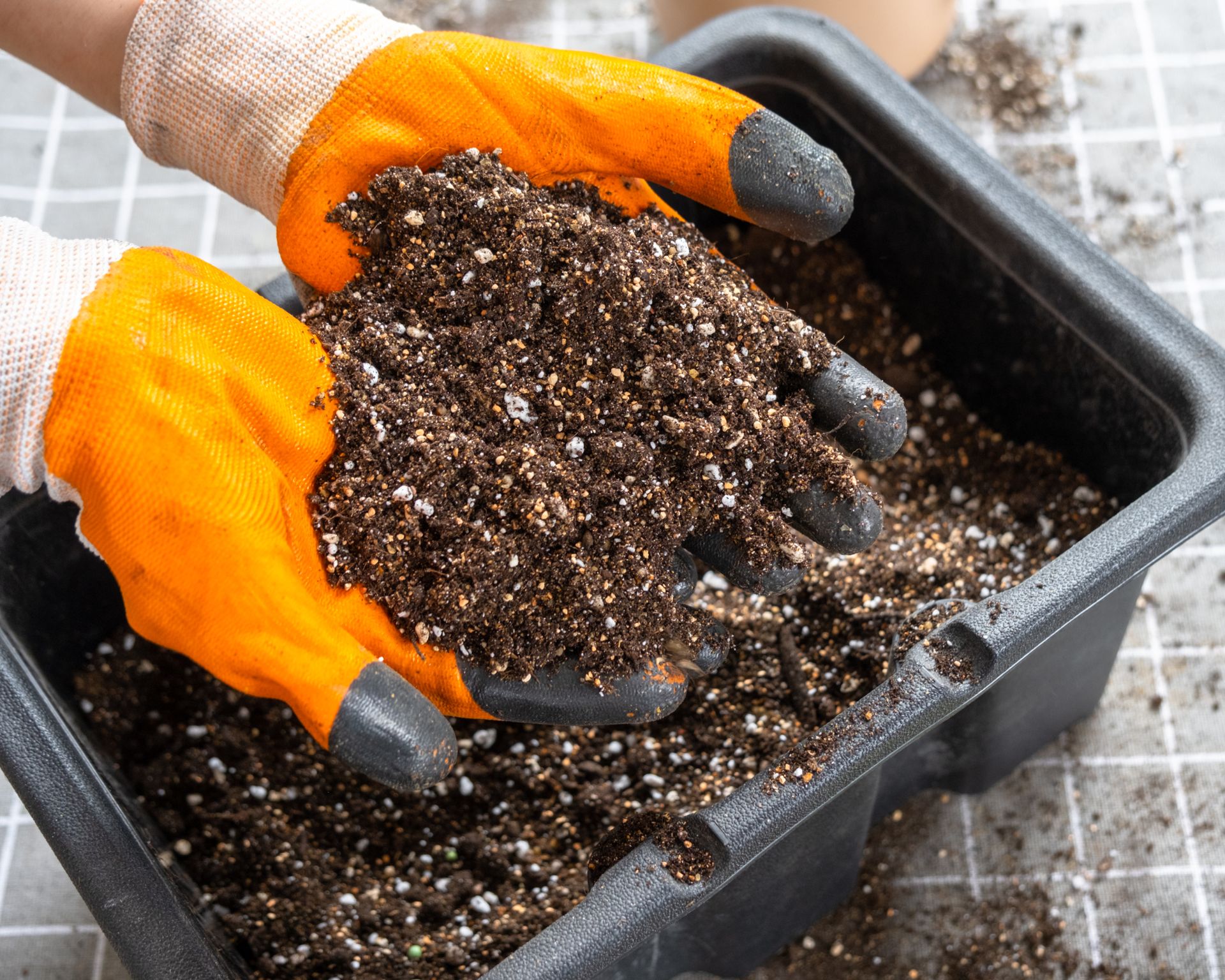 person wearing gloves mixing vermiculite into potting soil to improve moisture and nutrient control for container gardening
