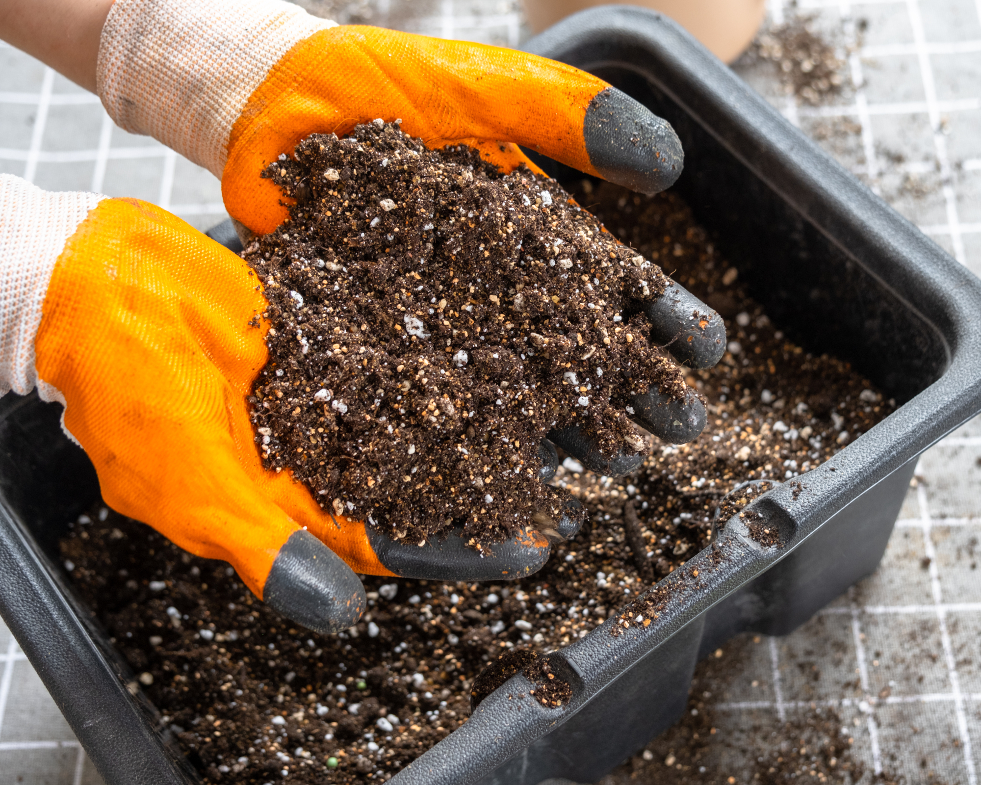 person wearing gloves mixing vermiculite into potting soil to improve moisture and nutrient control for container gardening