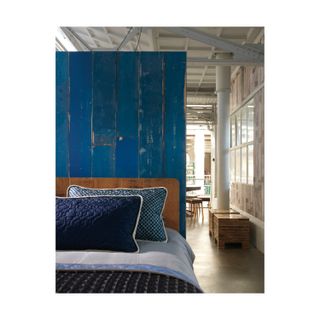 NLXL Blue Scrapwood Wallpaper in warehouse with leather upholstered bed frame and blue matching cushioning