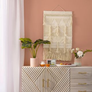 Pink room with pale wood sideboard and cream textured wall hanging above