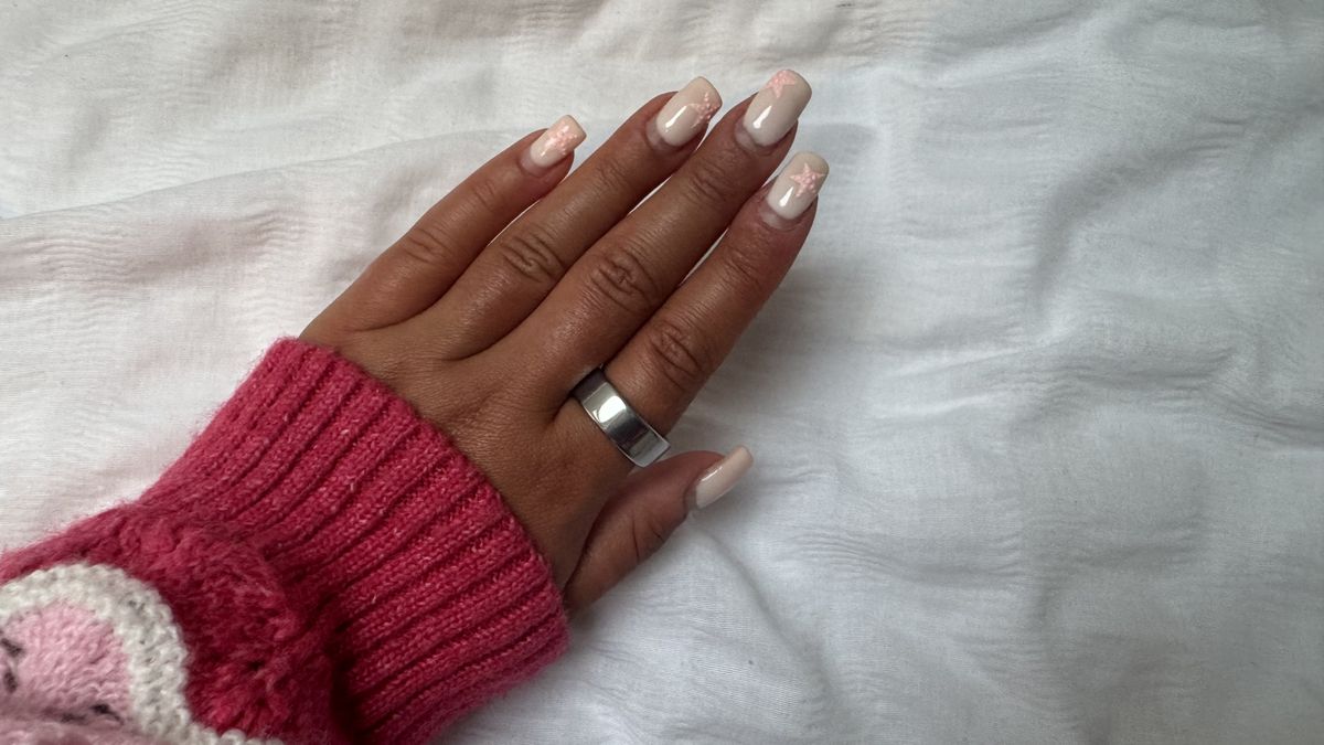 A woman's hand with pink nails and a pink sleeve wearing the Oura Ring 4