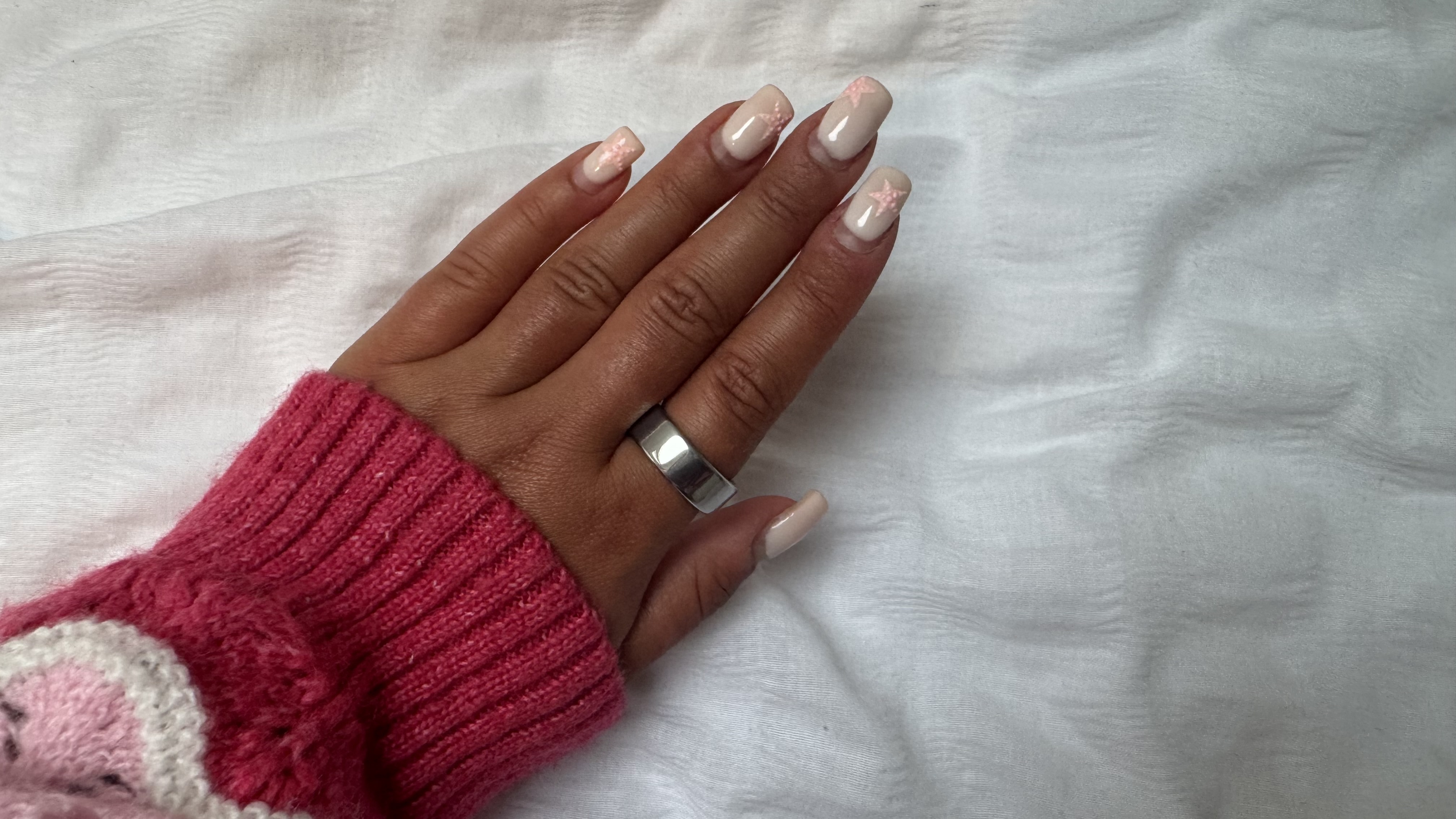 A woman's hand with pink nails and a pink sleeve wearing the Oura Ring 4