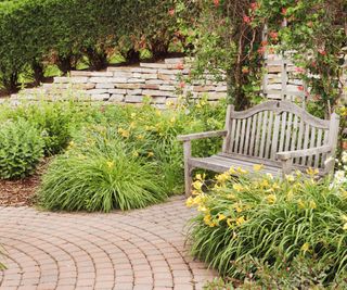 A wooden bench in a garden with a brick patio