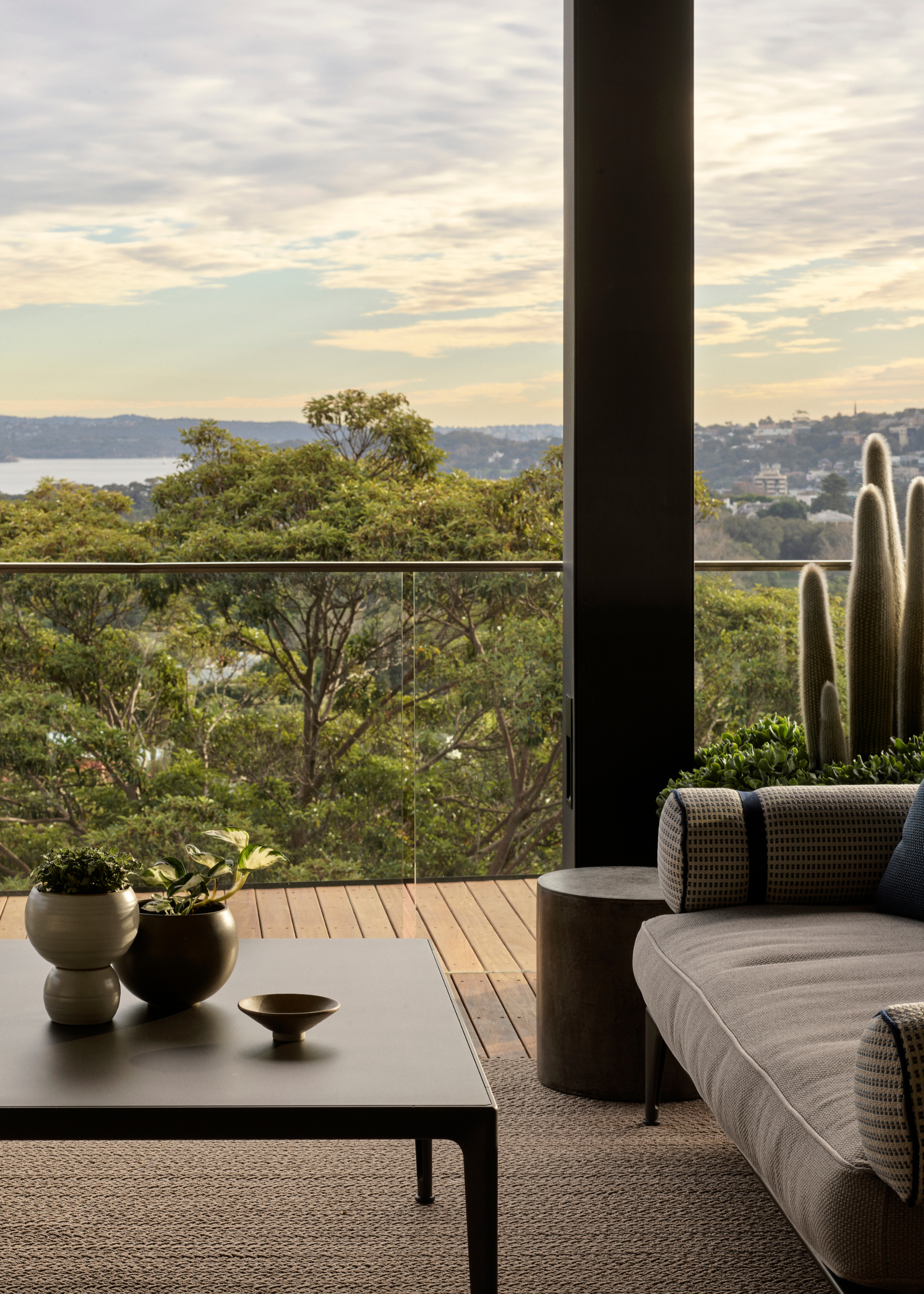 A balcony with a large rug, wood panelled flooring, a sofa seat and potted cacti