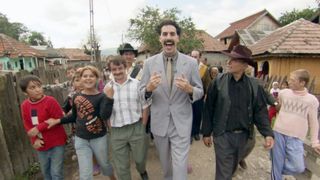 Borat walks among people from his home as he presents his documentary to the camera