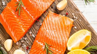 raw salmon on wooden chopping board with quarters of raw lemon