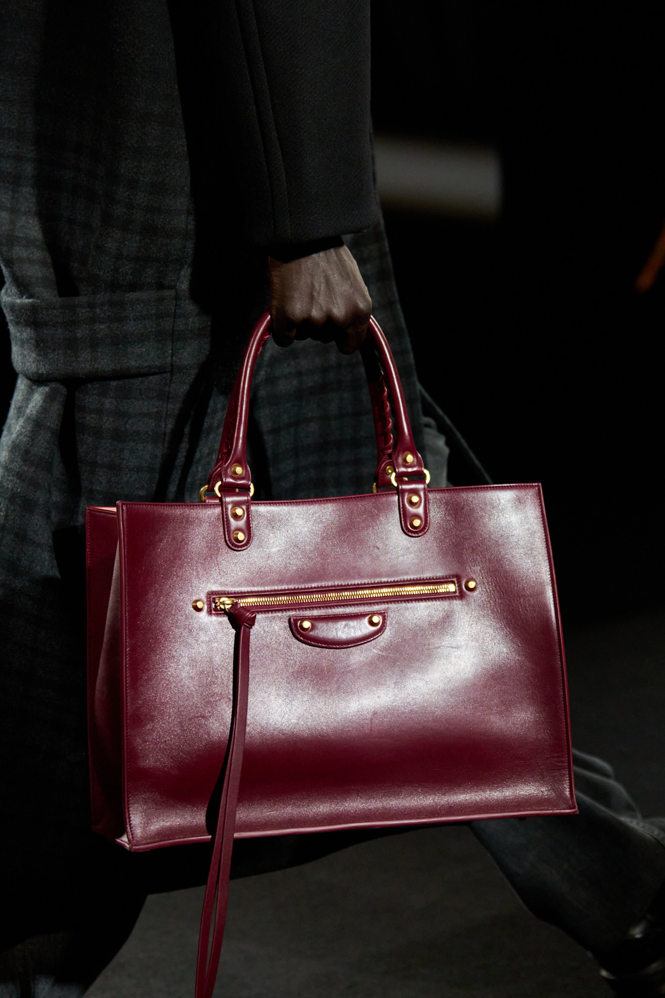 A close-up shot of a model walking in the Balenciaga F/W 26 show during Paris Fashion Week carrying a burgundy tote bag.