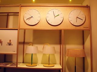 A wooden shelf display with 3 clocks showing different times, and table lamps below