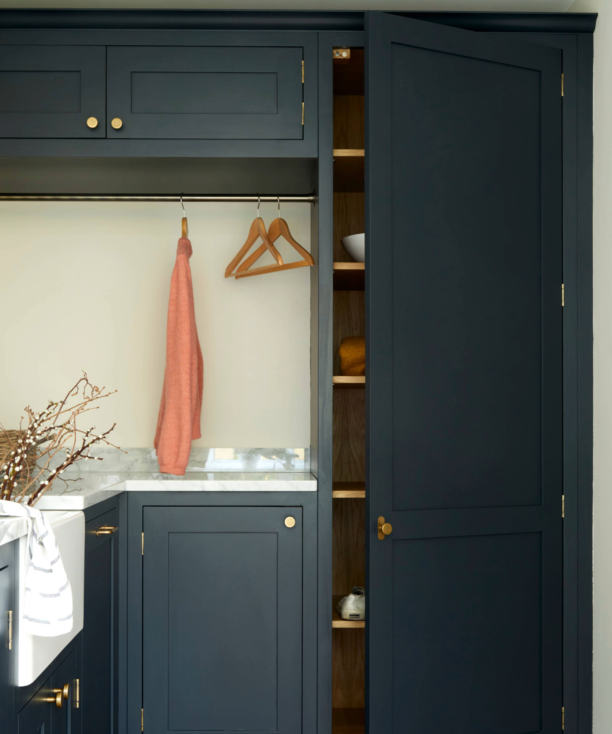 Utility room with dark blue cabinets and a hanging area next to an open shelved cupboard