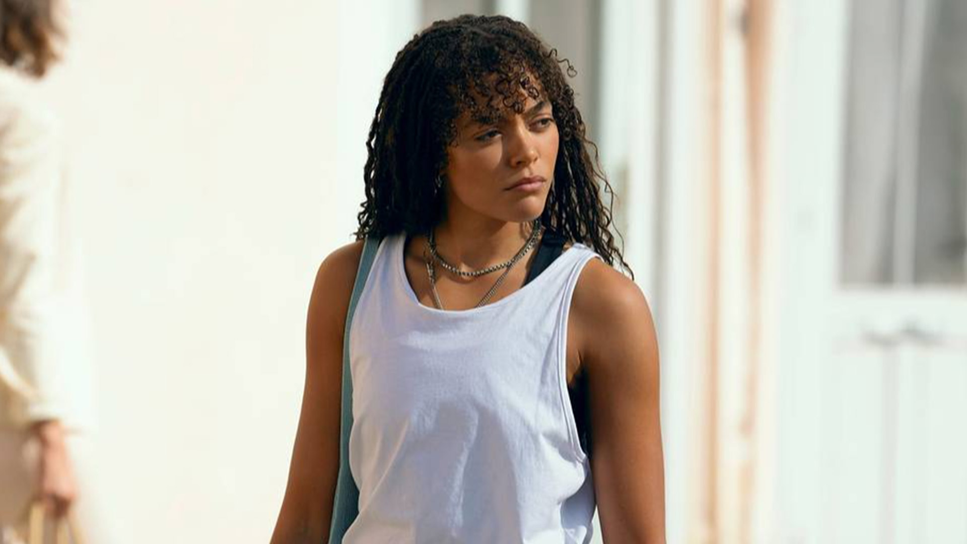 A woman wearing a white tank top looks over her shoulder 