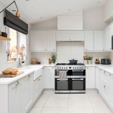 White painted kitchen with white cabinets and white tiled flooring, with an oven in the middle