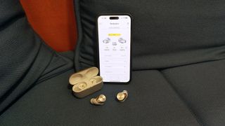 An iPhone on a sofa with the Technics Connect app on screen, with a pair of Technics earbuds next to it